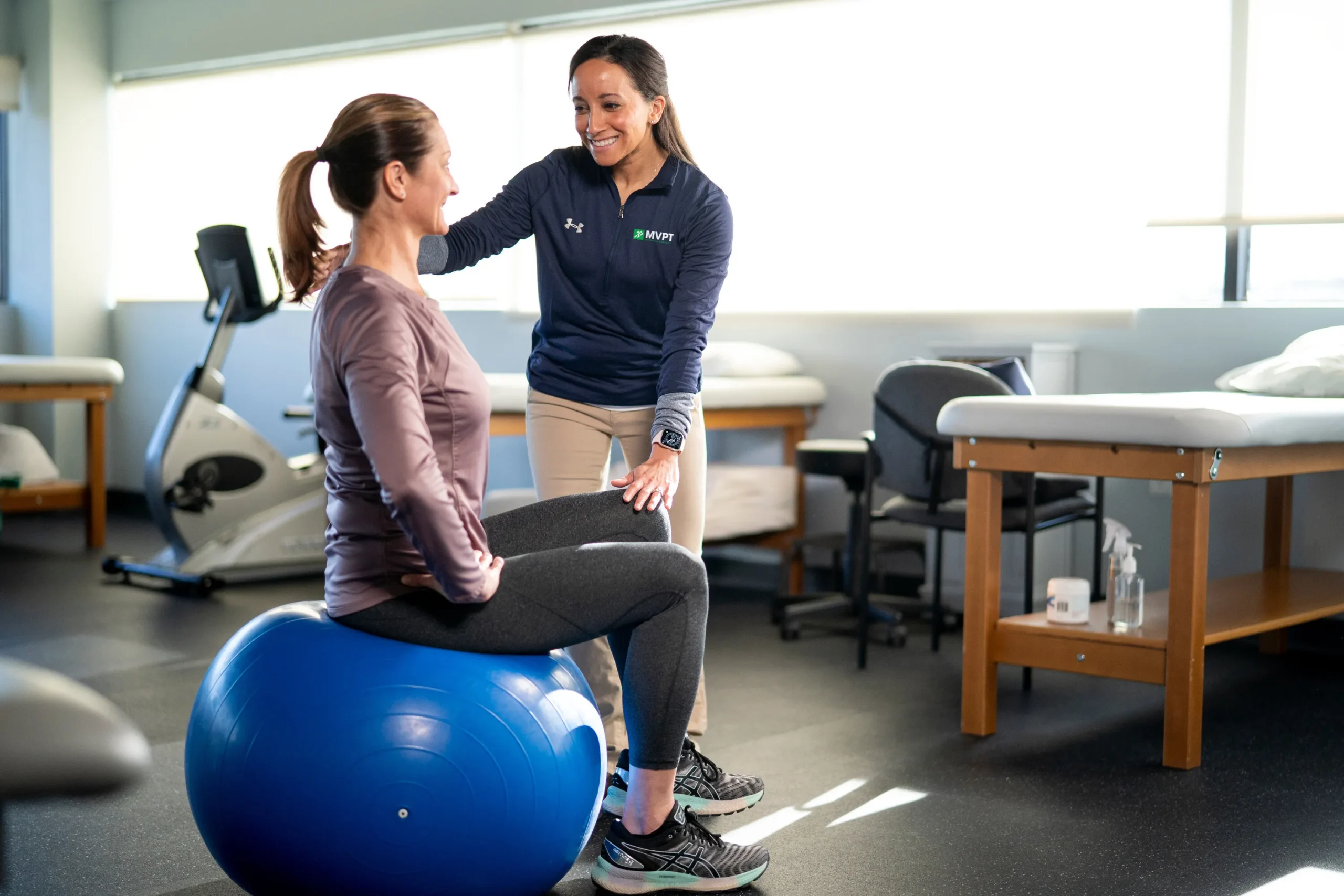 A woman engages in therapy on an exercise ball, supported by a physical therapist for her recovery journey.