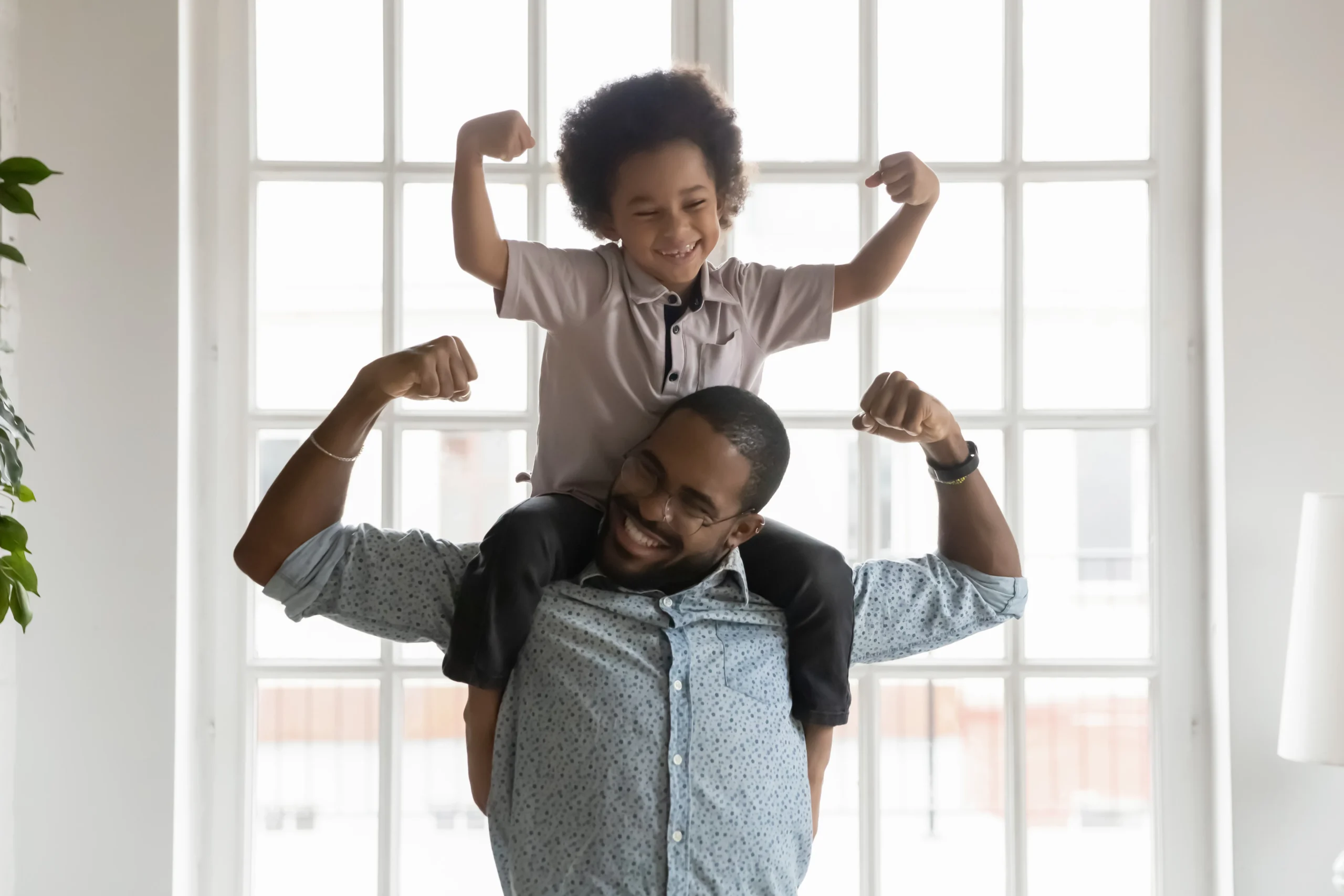 father and child on his shoulders flexing bicep muscle and laughing. 