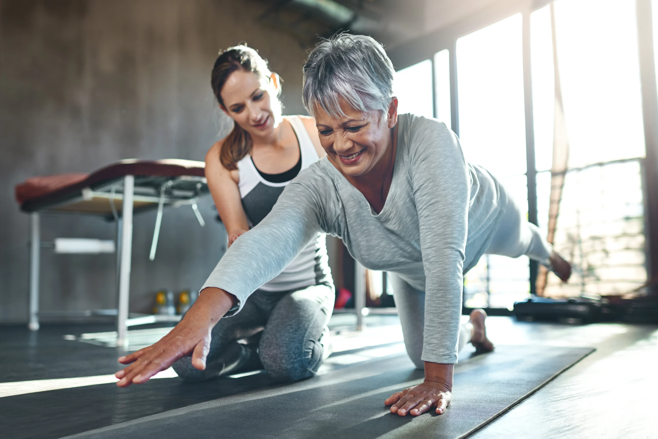 Two women, one younger the PT and one older the patient engaged in a yoga session, emphasizing physical activity for osteoporosis management.